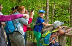 Besuchergruppe mit Kindern auf Aussichtsplattform: Frau schaut durch Fernglas, Kind steht am Geländer, Guide zeigt etwas